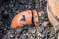 Cracked orange sewer pipe buried in gravel and dirt