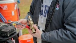 Person holding plumbing tools and a brass valve fitting, preparing to tighten the connection outdoors—often essential when troubleshooting sudden drops in water pressure.