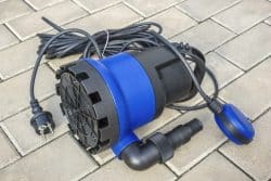 A blue and black submersible water pump with a power cord and float switch, placed on a paved surface—ideal for reducing plumbing risks during power outages.