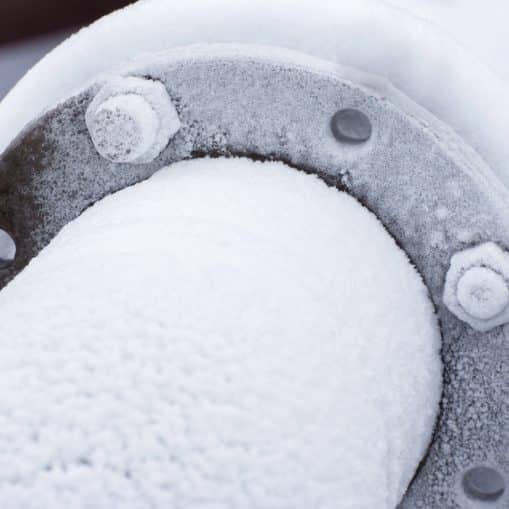 A close-up of a metal pipe and flange covered with frost and ice, illustrating how East Tennessee weather impacts plumbing during cold snaps.