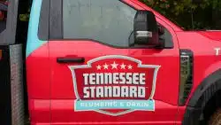 Red truck with "Tennessee Standard Plumbing & Drain" logo on the door, photographed outdoors on a rainy day.