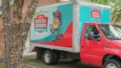 A red and white box truck with "Tennessee Standard Plumbing & Drain" branding, experts in fixing inconsistent hot water in Knoxville, is parked next to a tree and a brick building.