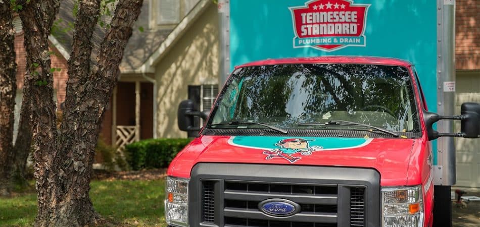 A Tennessee Standard Plumbing & Drain truck, specializing in professional drain cleaning in Maryville, is parked in front of a residential house with trees and grass in the foreground.