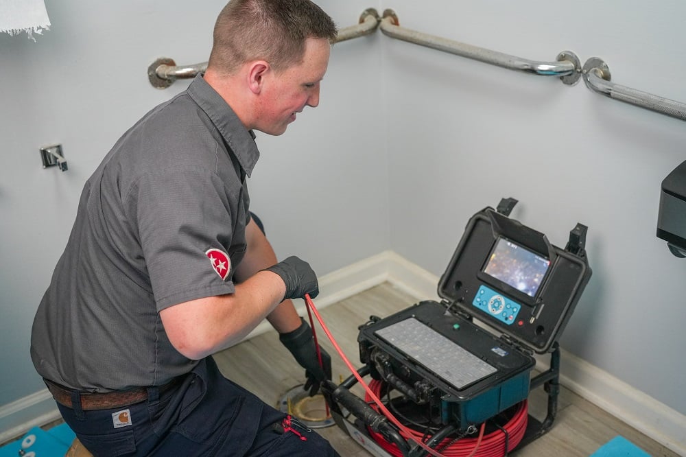 A technician uses a video inspection device to examine plumbing in a bathroom, viewing footage on a monitor—an essential step before drain cleaning in Knoxville.