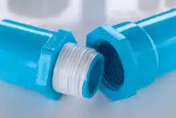Close-up of two blue PVC pipe fittings with white Teflon tape wrapped around the threaded connection.