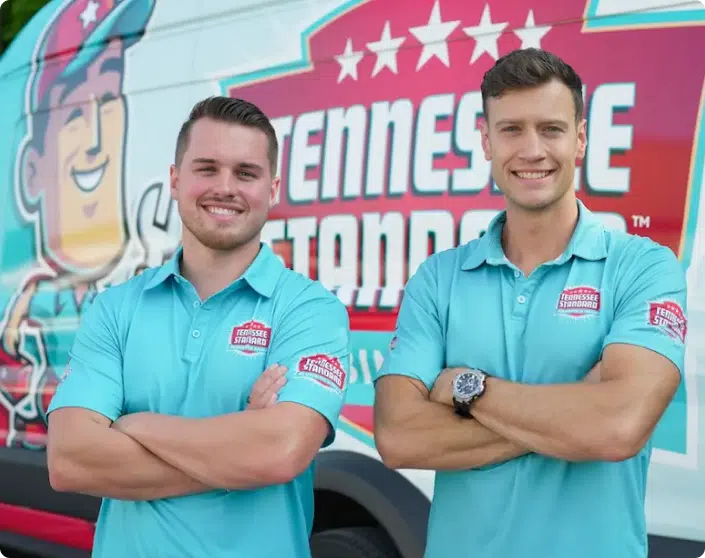 Two men in matching turquoise polo shirts stand with arms crossed in front of a van featuring a cartoon and the words