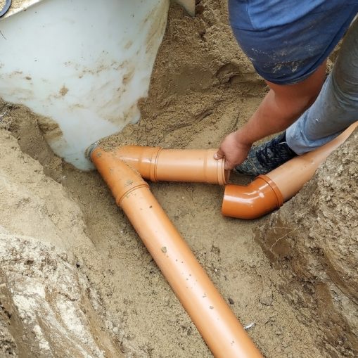 Worker installing orange sewer pipes in a dug trench