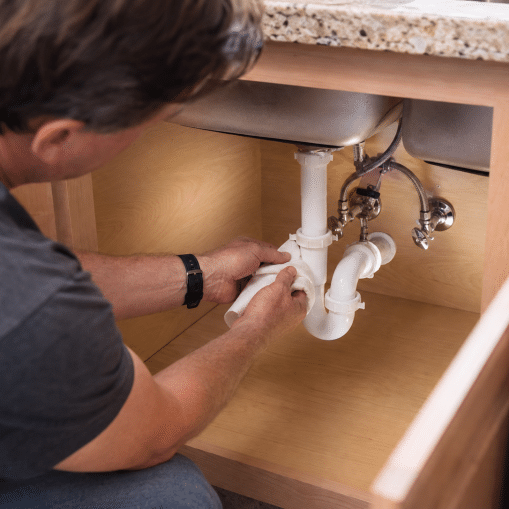 a Knoxville homeowner in casual home attire performing a simple monthly plumbing check under a kitchen