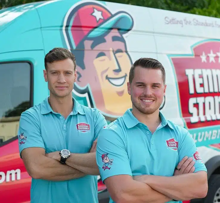 Bobby and Kelton Balka in light blue shirts stand smiling with arms crossed in front of a van displaying the Tennessee Standard logo and colorful graphics.