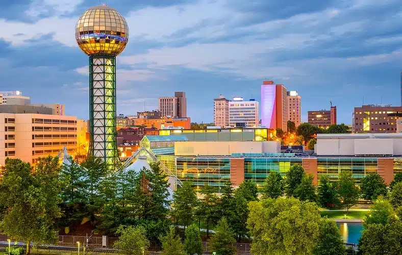 Cityscape of Knoxville, Tennessee, featuring the Sunsphere tower and downtown buildings under a cloudy sky.