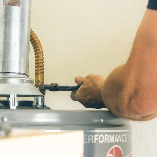 Person using a wrench to adjust a pipe connection on top of a water heater, addressing issues like inconsistent hot water in Knoxville.