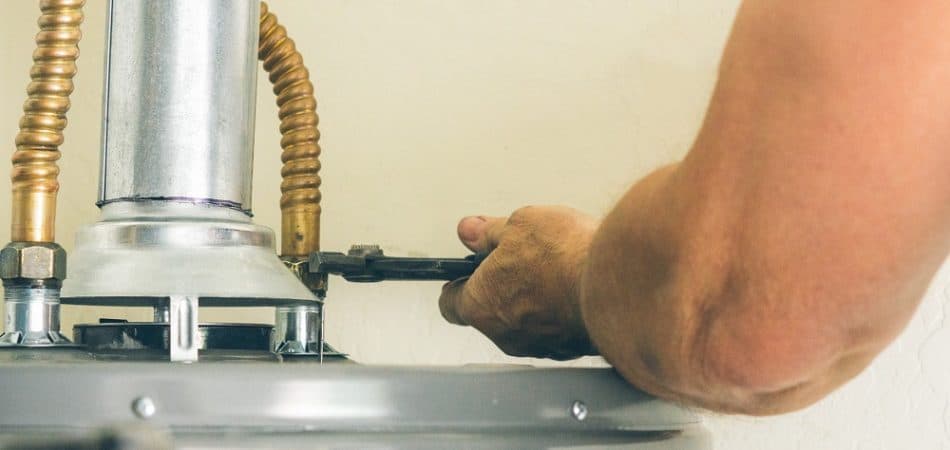 Person using a wrench to adjust a pipe connection on top of a water heater, addressing issues like inconsistent hot water in Knoxville.