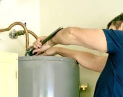 Person using a wrench to adjust piping on top of a gray water heater mounted against a wall, ready to solve issues like hot water runs out fast in Maryville.