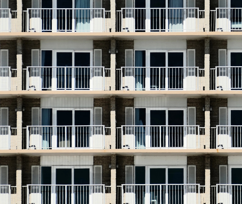 A symmetrical facade of a building with multiple identical balconies and glass doors arranged in a grid pattern.