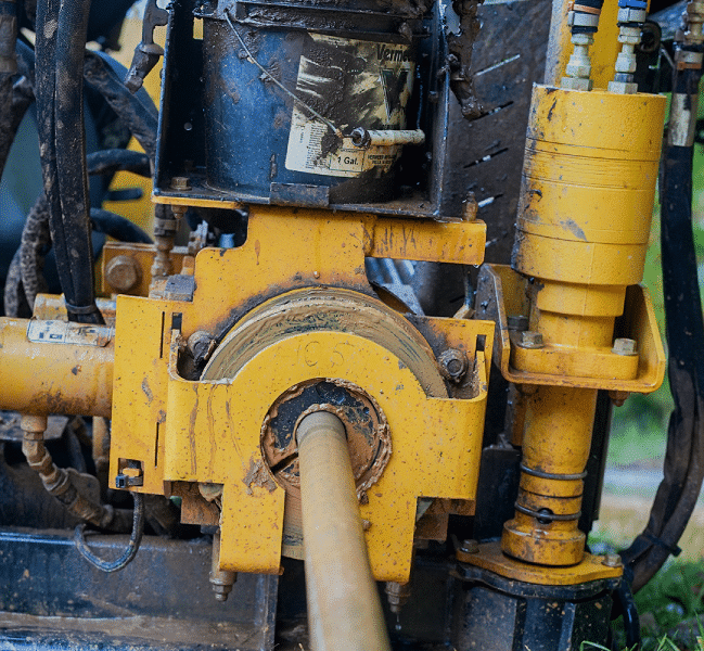 Close-up of a muddy yellow mechanical drill with cylindrical components and greasy surfaces.