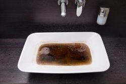 A white rectangular sink filled with dark, murky water sits below a chrome faucet and soap dispenser on a dark countertop—an obvious sign that Drain Cleaning in Knoxville is needed.