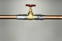 A brass valve on a copper pipe wrapped with duct tape struggles against high water pressure, leaking droplets onto a plain background.