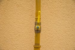 Yellow gas valve with a lever handle attached to a vertical yellow pipe, part of the gas line for an outdoor kitchen in Maryville, mounted against a textured beige wall.