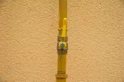 Yellow gas valve with a lever handle attached to a vertical yellow pipe, part of the gas line for an outdoor kitchen in Maryville, mounted against a textured beige wall.