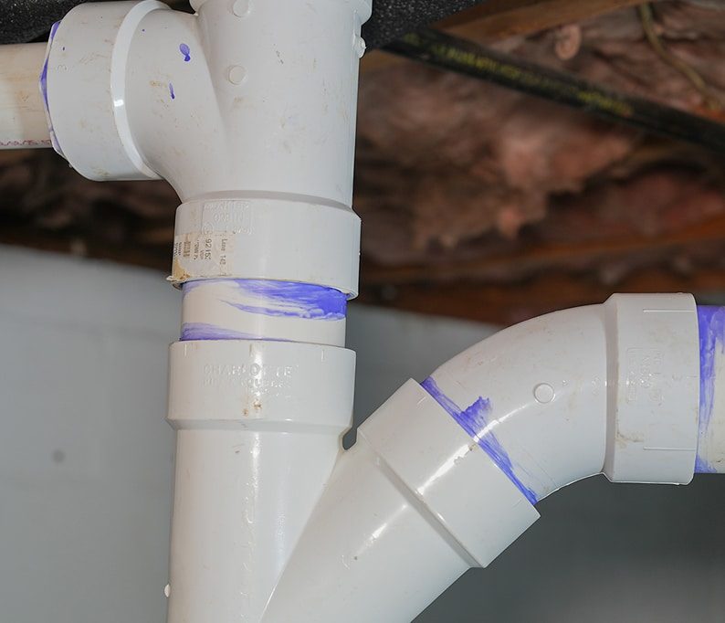 Close-up of white PVC plumbing pipes connected with blue solvent weld marks visible at the joints.