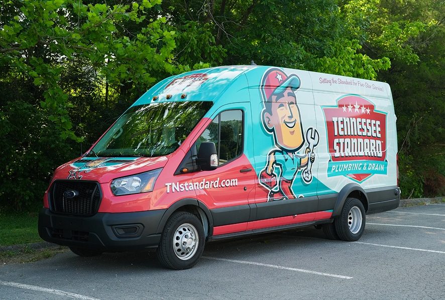 A branded van for The Tennessee Standard is parked in a lot, featuring a cartoon character holding a wrench on its side.