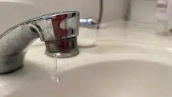 A close-up of a bathroom faucet with a small stream of water dripping into a white sink.