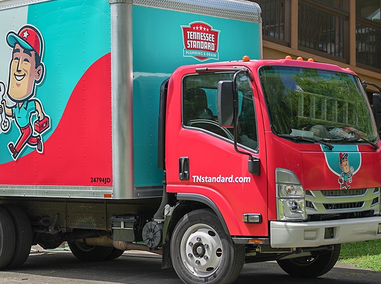 A red and teal delivery truck with a cartoon character graphic, parked on a residential street.