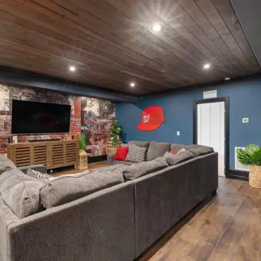 A finished basement living room with a sectional sofa, wall-mounted TV and recessed lighting