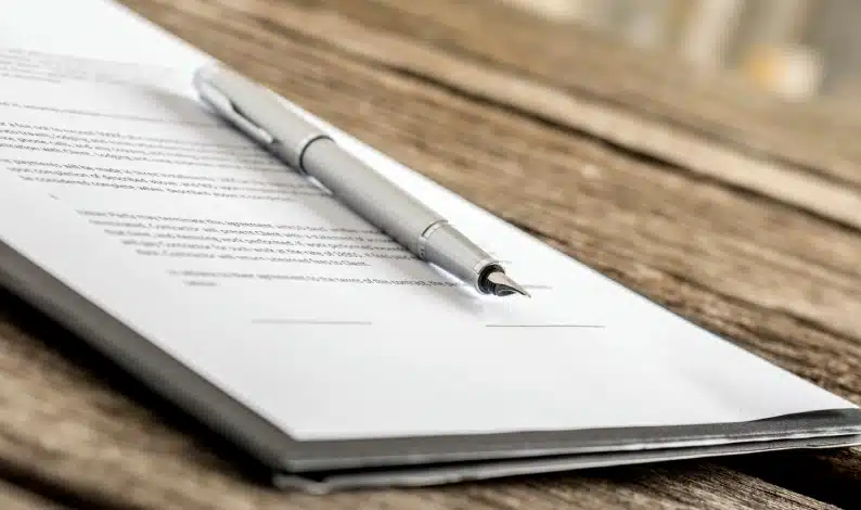 A silver pen rests on top of a stack of papers with printed text, placed on a wooden surface.