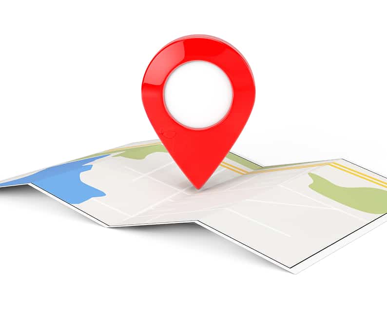 A red map pin marker is placed on a folded paper map with visible roads and colored areas indicating land and water.