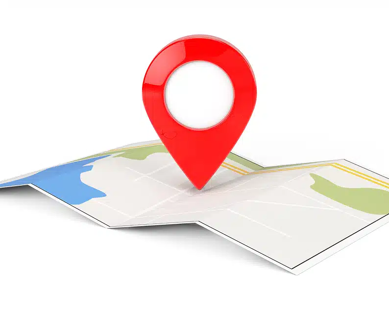 A red map pin marker is placed on a folded paper map with visible roads and colored areas indicating land and water.