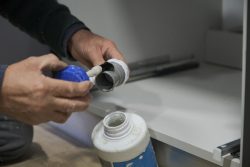 Mature plumber hands applying glue to a grey plastic pipe. Repairman working.
