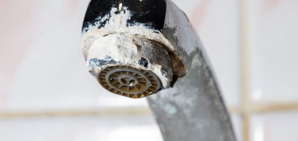 Close-up of a metal faucet with significant white mineral buildup and corrosion, highlighting common white buildup on faucets in Maryville, set against a tiled background.
