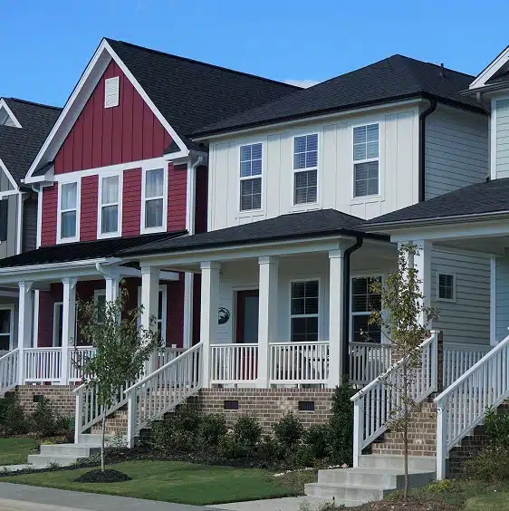 Row of modern two-story houses with front porches, brick steps, and neatly landscaped yards under a clear blue sky.
