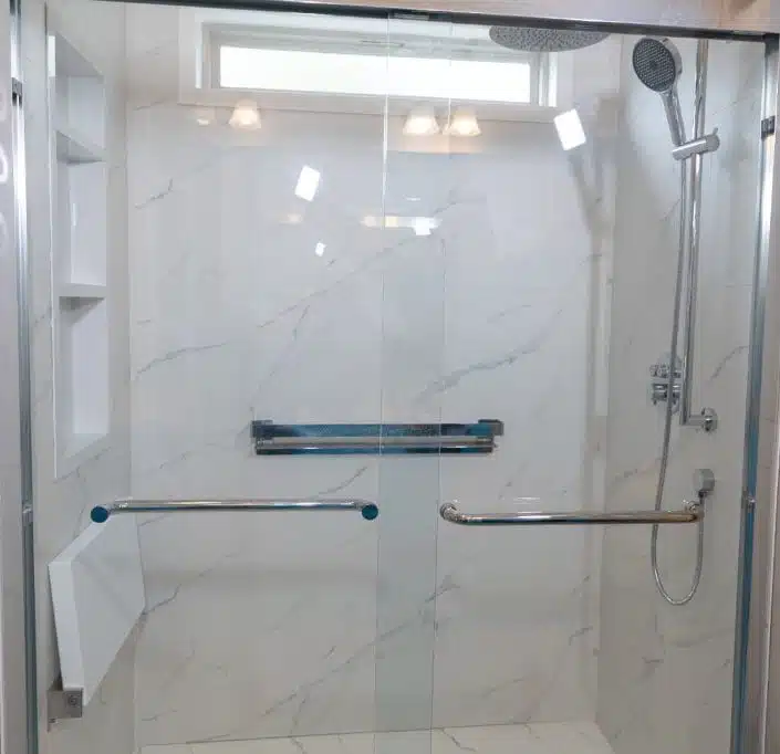 walk-in shower featuring a frameless glass door, white marble-style tiled walls, and built-in shelving