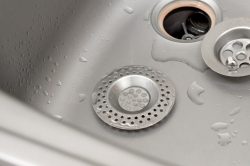 Close-up of a kitchen sink with water droplets, featuring a metal drain strainer and removed drain cover—ideal for illustrating the process of installing kitchen sink drain components.
