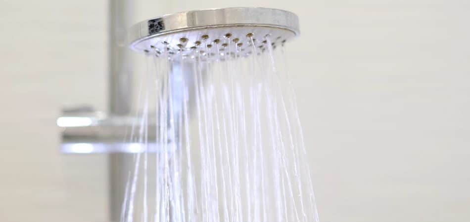 Close-up of a modern handheld showerhead spraying water, mounted on a metal rail against a plain background—a common sight when hot water runs out fast in Maryville.