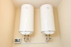 Two white wall-mounted water heaters with pipes and a control panel are installed on a beige wall—ideal for addressing inconsistent hot water in Knoxville homes.