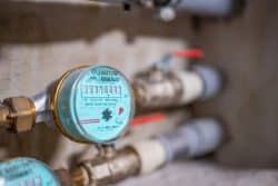 Close-up of a water meter with visible numbers and plumbing pipes attached, installed on a wall.