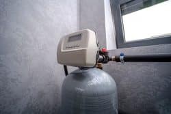 A water softener unit with a digital control panel sits atop a gray tank.