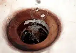 Close-up of a dirty sink drain with water droplets splashing and visible rust or stains around the opening, often a sign of clogged drains in Maryville.