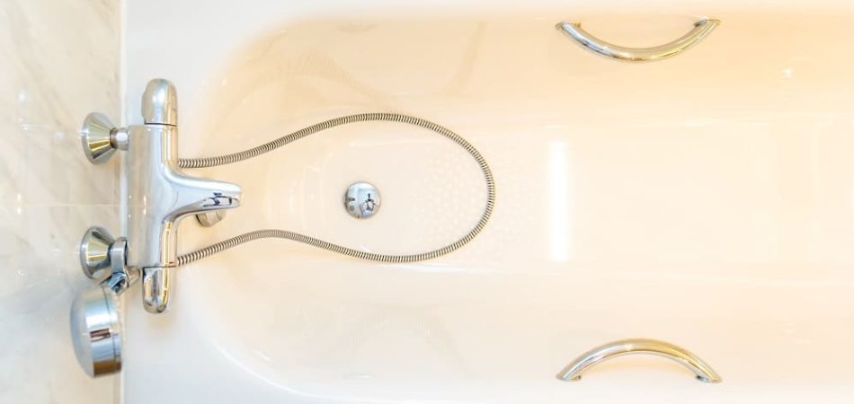 Overhead view of an empty white bathtub with chrome handles, a silver faucet, and a flexible shower hose resting inside near the bathtub drain.