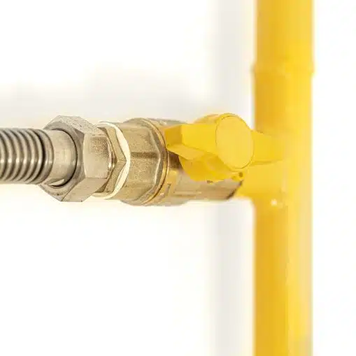 Close-up of a yellow gas valve connected to a metal pipe and flexible hose, part of a gas line for an outdoor kitchen in Maryville, mounted on a white wall.